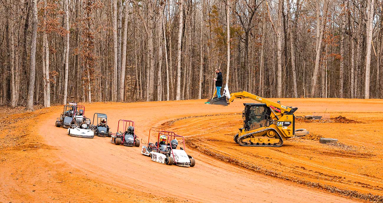 Team members race go-karts in front of a makeshift flagstand at the Niece Motorsports dirt track