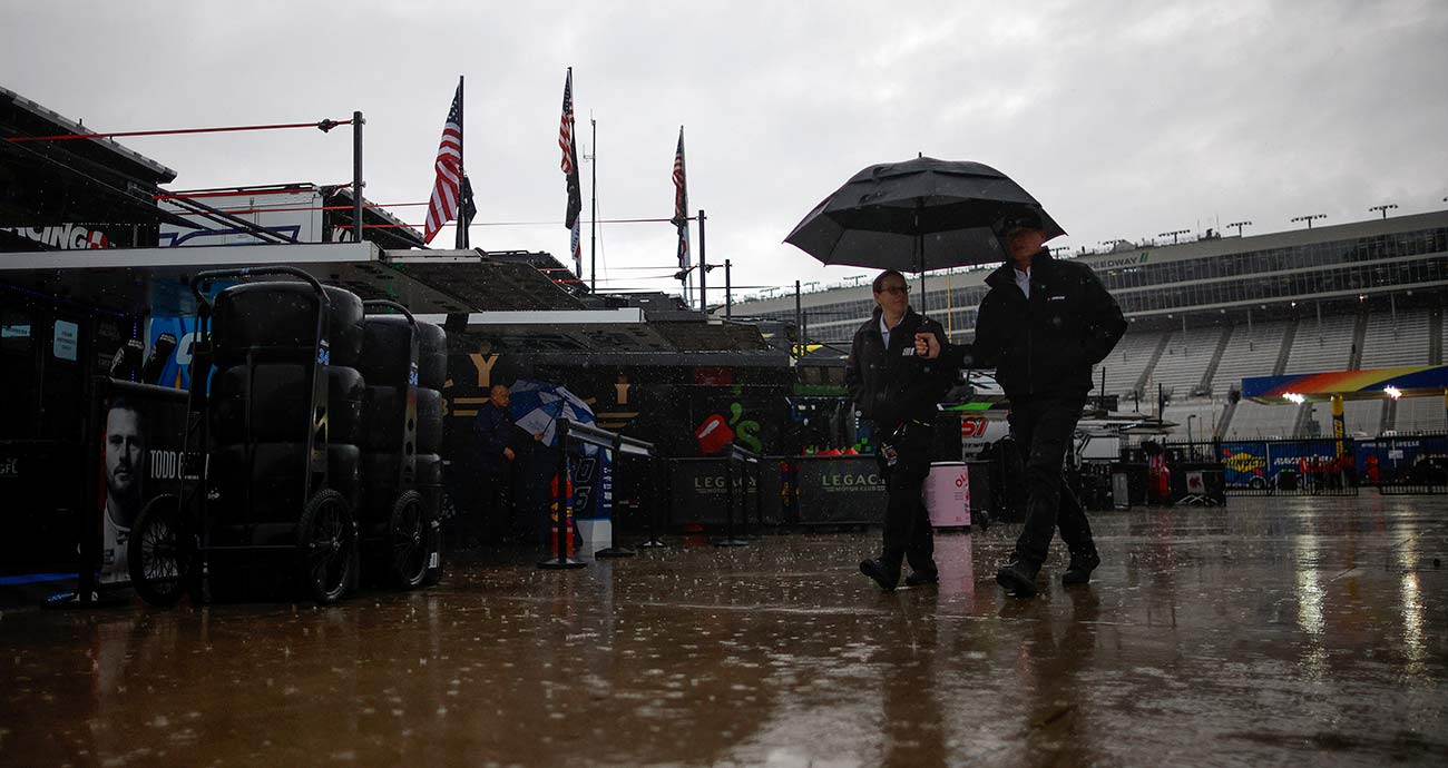 NASCAR officials walk with an umbrella for cover through the Cup Series garage area at EchoPark Speedway