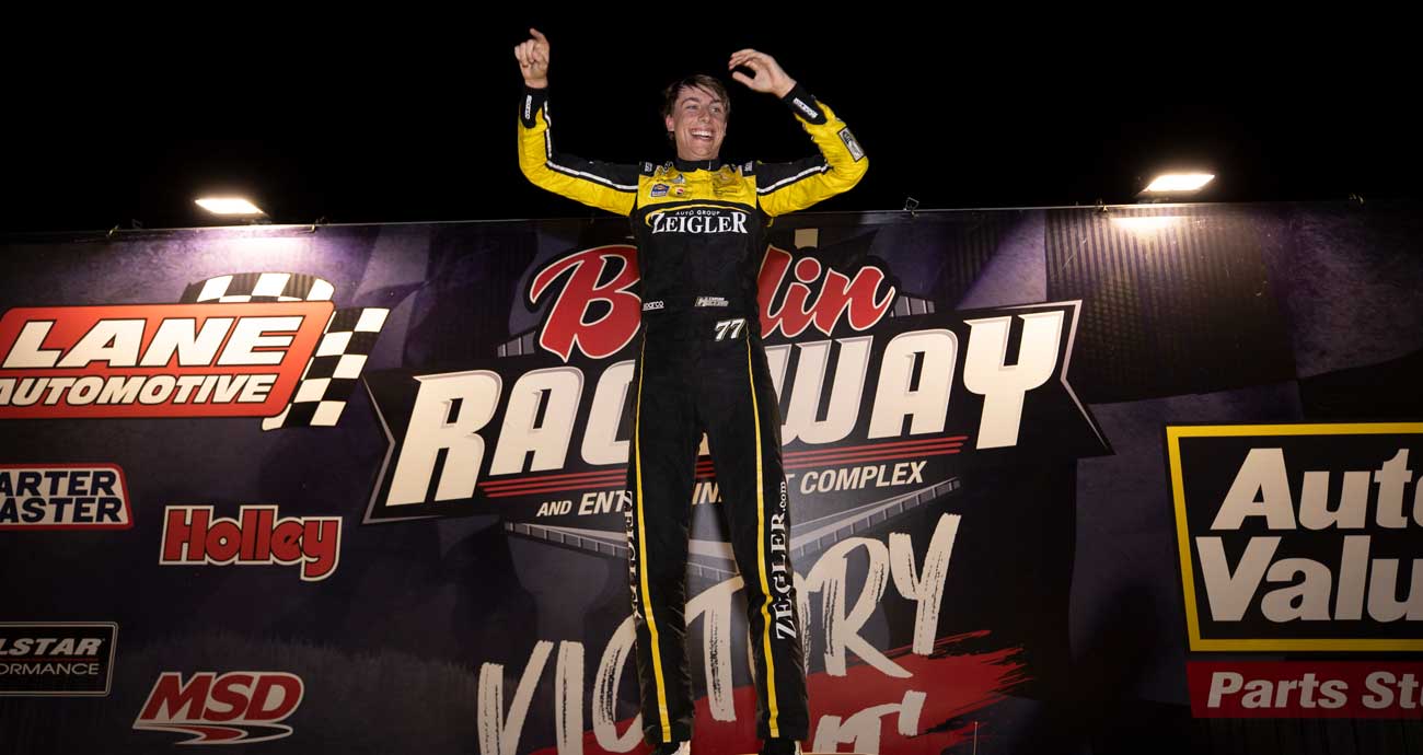 Carson Hocevar stands on his car, celebrating a win at Berlin