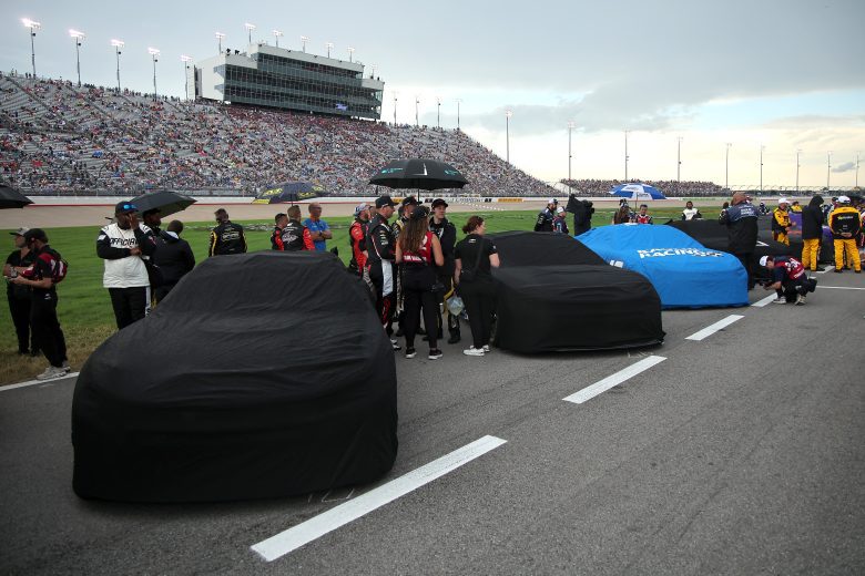 NASCAR cars sit on pit road with covers on.