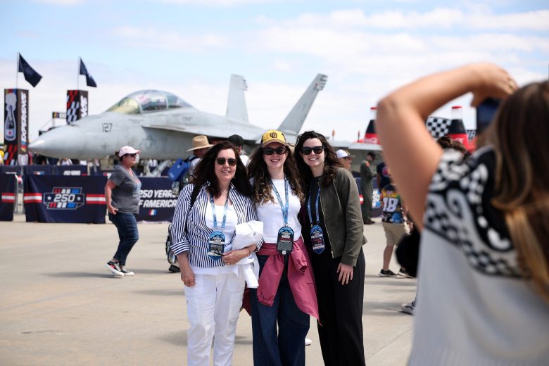 Fans pose for photos in front of a fighter jet.
