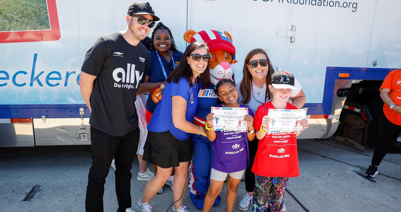 Driver Alex Bowman and The NASCAR Foundation's Nichole Krieger pose with kids who won events at the Speediatrics Fun Day Festival at Naval Base Coronado.