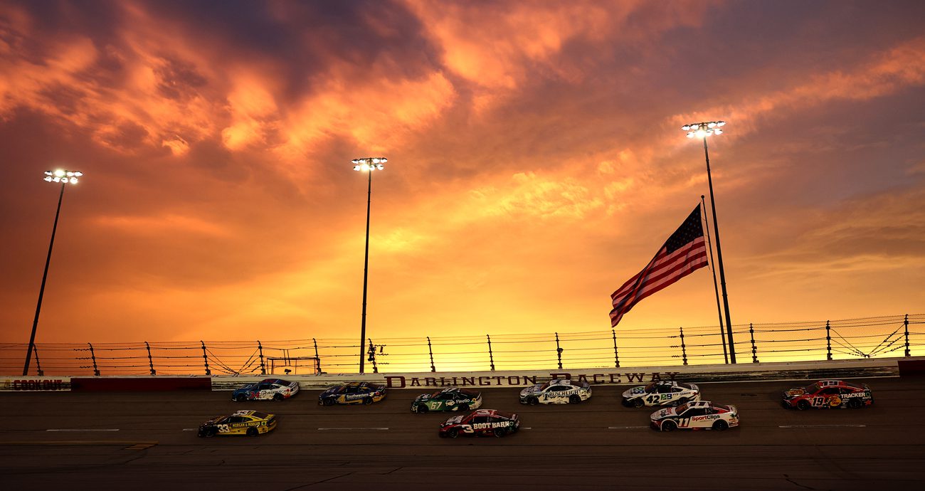 Sunset at Darlington Raceway with cars on track in the foreground.